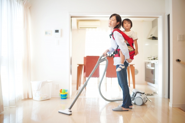 子どもをおんぶして大変そうに掃除をしている母親